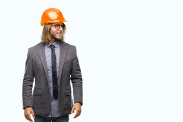 Young handsome architec man with long hair wearing safety helmet over isolated background looking away to side with smile on face, natural expression. Laughing confident.