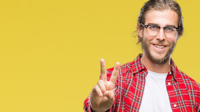 Young handsome man with long hair wearing glasses over isolated background smiling looking to the camera showing fingers doing victory sign. Number two.
