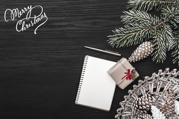On a black background, a fir tree with cone and decorative objects. Gift and a note book or for a winter holiday message. Top view.