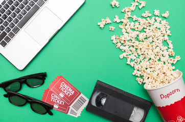 Movie time, flat lay with space for text. Cinema minimal concept. Composition on a green background with a laptop, VHS cassette, 3d glasses, movie tickets and popcorn