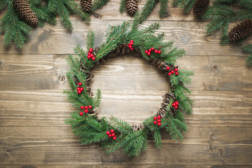 Christmas wreath made of spruce branches with holly berries on wooden board. Flat lay. Top view.