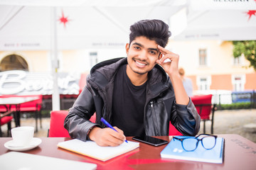 Young stylish indian man city in cafe in city writing notes in book