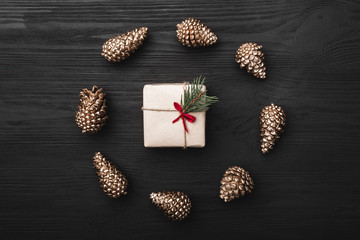 Upper, top view, of Christmas presents on a wooden black rustic background, suround by circle of golden pine cones