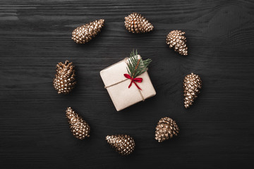 Upper, top view, of Christmas presents on a wooden black rustic background, suround by circle of golden pine cones