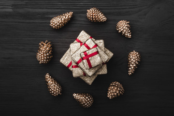 Upper, top view, of Christmas presents on a wooden black rustic background, suround by circle of golden pine cones