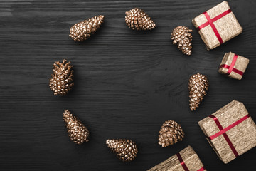 Upper, top view, of Christmas presents on a wooden black rustic background, with space for text writing and golden pine cones.