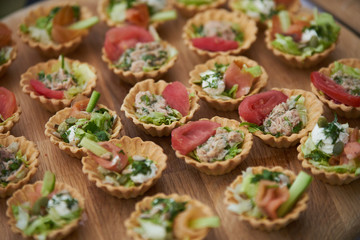 Tartlets with vegetables, chicken breast, cream and a slice of tomato on a wooden table.