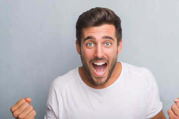 Handsome young man over grey grunge wall screaming proud and celebrating victory and success very...