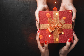On a black background, a man's hands carry a gift in the hands of a young lady. Effect of light...