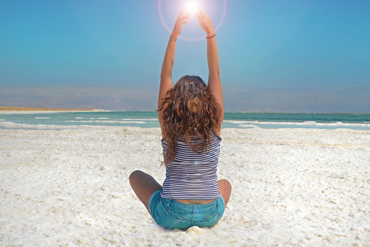 young girl with her hands is catching the energy of the sun. long-haired girl sits on the shore of the Dead Sea in Israel.