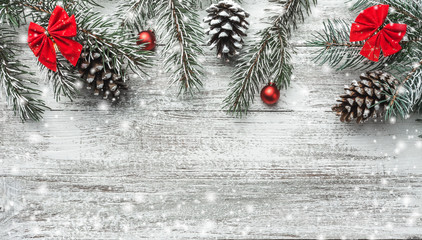 Christmas theme with fir branches, cones, globes, red bows on white wooden background viewed from above, in snow, greeting card with space for text