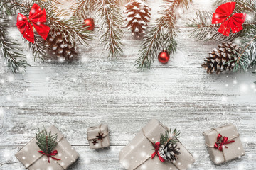 Christmas theme with fir branches, cones, globes, red bows, present boxes on white wooden background viewed from above, in snow, greeting card with space for text