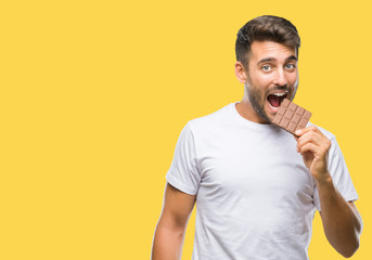 Young handsome man eating chocolate bar over isolated background with a confident expression on...