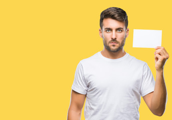 Young handsome man holding blank card over isolated background with a confident expression on smart face thinking serious