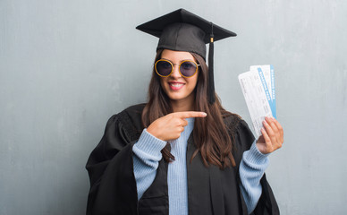 Young brunette woman over grunge grey wall wearing graduate uniform holding boarding pass very...