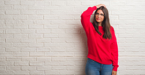 Young brunette woman standing over white brick wall confuse and wonder about question. Uncertain...