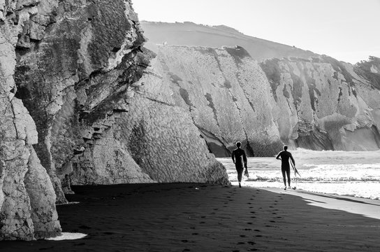 surfers walking on the beach in black and white