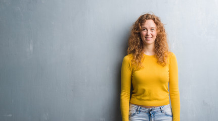 Young redhead woman over grey grunge wall with a happy and cool smile on face. Lucky person.