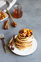 Stack of delicious sweet and spicy apple pancakes with fried caramelized apples, anise, cinnamon and honey on a white plate. Autumn breakfast. Copy space.