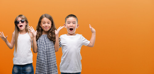 Group of boy and girls kids over orange background very happy and excited, winner expression...