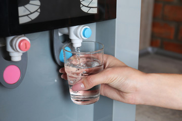 Woman filling glass from water cooler, closeup