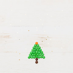 Top view on a funny Christmas tree made of candies with small golden stars confetti on white wooden background. Winter, Christmas and Happy New Year concept