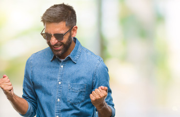 Adult hispanic man wearing sunglasses over isolated background very happy and excited doing winner gesture with arms raised, smiling and screaming for success. Celebration concept.
