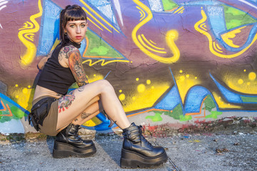 tattooed rebel girl posing against a wall painted