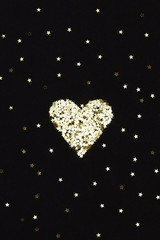 Closeup of golden heart made of small stars on black background. Winter, Christmas celebration, holidays season concept