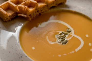 Macro view of pumpkin and carrot soup bowl, with freshly baked Belgian waffle