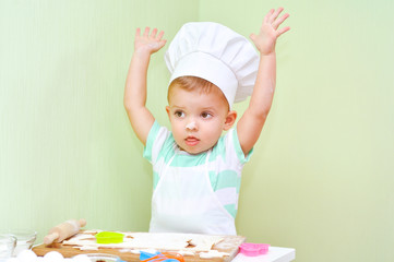 A little baker in a white suit chef bakes cookies from the dough