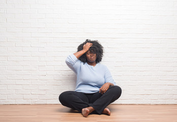 Young african american woman sitting on the floor at home suffering from headache desperate and stressed because pain and migraine. Hands on head.