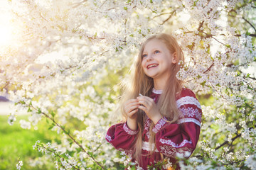 Lovely lttle girl stands under a blooming plum in park in ethnic ukrainian dress