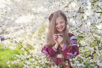 Lovely lttle girl stands under a blooming plum in park in ethnic ukrainian dress