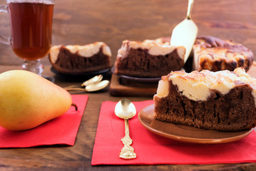 Cut pieces of cake spread out on a metal spatula plates, ripe pear on a red napkin, a glass of tea on a wooden background.