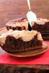 Unfolding chocolate cake with a curd layer on a plate with a spatula of metal.