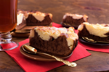 Pieces of chocolate dough cake with a curd layer, spread out on dessert plates, red napkins on a wooden background, a glass of tea.