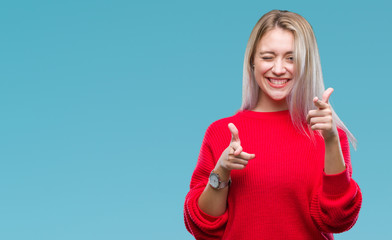 Young blonde woman wearing winter sweater over isolated background pointing fingers to camera with happy and funny face. Good energy and vibes.