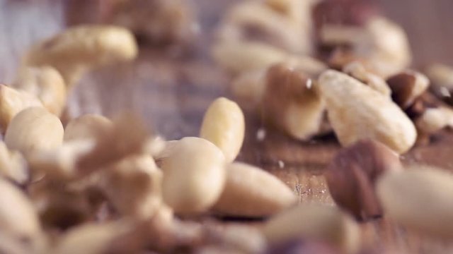 Different types of raw nuts dropping on wooden table. Ingredients of superfood breakfast. 