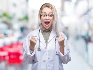 Young blonde doctor woman over isolated background celebrating surprised and amazed for success with arms raised and open eyes. Winner concept.