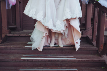 The bride is holding the hem of the wedding dress. Beige dress with lace. Shoes, tights for the...
