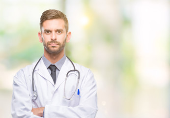 Young handsome doctor man over isolated background skeptic and nervous, disapproving expression on face with crossed arms. Negative person.