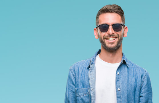 Young handsome man wearing sunglasses over isolated background looking away to side with smile on face, natural expression. Laughing confident.