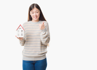 Young Chinese real state agent woman over isolated background holding house happy with big smile doing ok sign, thumb up with fingers, excellent sign