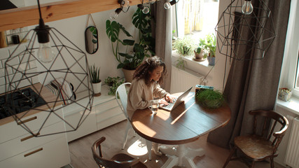 Charming young woman typing on laptop computer in a kitchen.