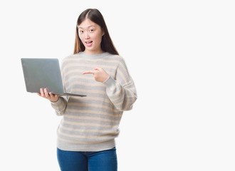 Naklejka premium Young Chinese woman over isolated background using computer laptop very happy pointing with hand and finger