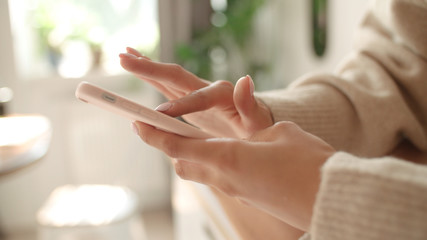 Close up of female hands using modern smartphone device at home.