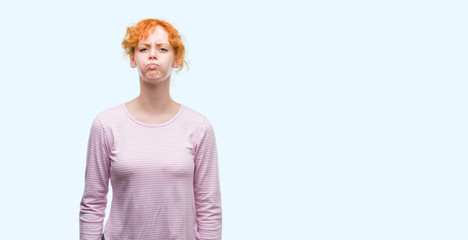 Young redhead woman puffing cheeks with funny face. Mouth inflated with air, crazy expression.