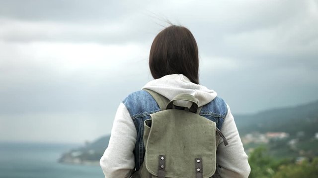 Rear view backpacker woman standing on top of mountain admiring seascape