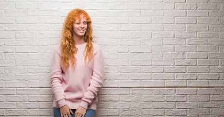 Young redhead woman standing over brick wall winking looking at the camera with sexy expression,...